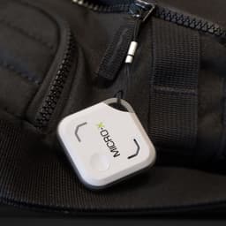A small white Bluetooth tracker attached to a black bag, featuring a clip and minimalistic design.
