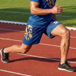 Men's active shorts in blue with a design feature, paired with black running shoes on a track surface.