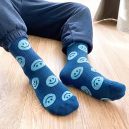 A pair of blue crew socks featuring smiling face patterns, with one sock slightly offset from the other.