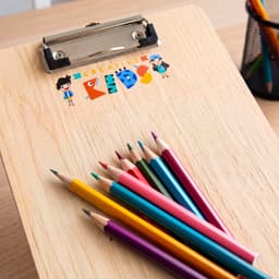 A wooden clipboard features a colourful logo and is surrounded by vibrant coloured pencils.