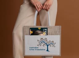 A jute canvas bag in natural and beige tones, featuring a logo and holding a magazine.