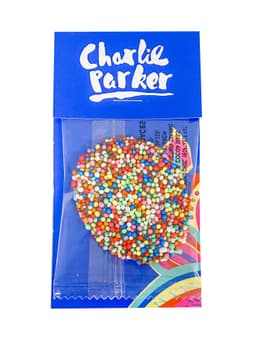 A chocolate freckle covered in colourful sprinkles, packaged in a blue cardboard sleeve with a logo.