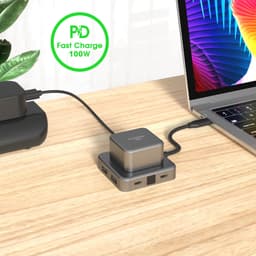 A USB hub in brushed aluminium with multiple ports, connected to a laptop on a wooden desk. Features a logo.