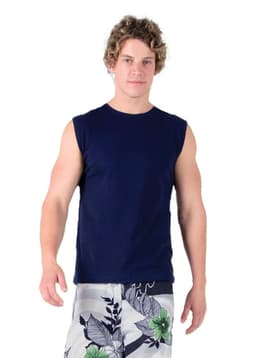 A man wearing a navy muscle T-shirt and floral shorts, standing on a grassy area with trees in the background.