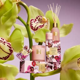 A collection of pink and floral-scented homewares, including a diffuser, candle, and soap, against a floral background.