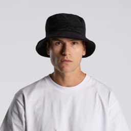 A black cord bucket hat worn by a model, paired with a plain white t-shirt. The hat features a branding logo.
