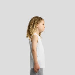 A child wearing a plain white singlet tank top, featuring curly hair, standing in profile against a neutral background.
