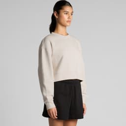 A light beige cropped jumper with long sleeves, paired with black shorts. The garment has a simple design and a logo.