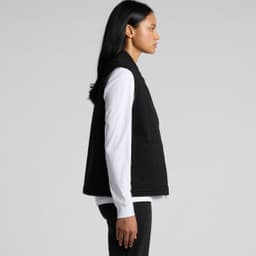 A black canvas heavy vest features a simple design with side pockets and a logo. Model wears a white shirt underneath.