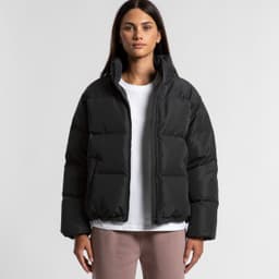 A puffer jacket in black, featuring a zip-up front and a casual, oversized fit. The model wears a white top underneath.