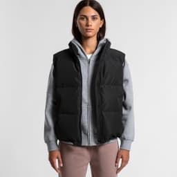 A black puffer vest worn over a grey hoodie, featuring a zip front and a logo. Model stands against a plain background.