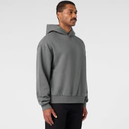 A grey hooded jumper with a relaxed fit, featuring a logo on the front. The model is standing sideways.
