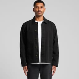 A man wearing a black canvas chore jacket with button closure and multiple pockets. The background is plain grey.
