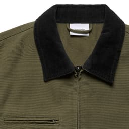 A close-up of an olive green jacket featuring a black cord collar and a zippered front. There is a small pocket on the chest.