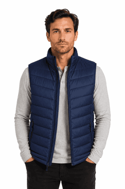 A man models a navy blue puffer vest over a light grey long-sleeve shirt, featuring a branded logo.