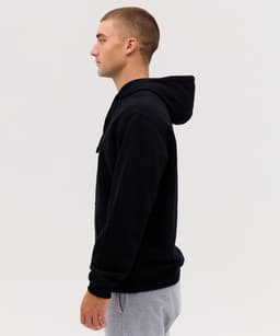 A black hoodie with a hood, displayed on a model in profile, paired with grey pants. The hoodie features a logo.