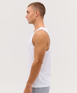 A white singlet displayed on a male model from the side. The model has short hair and is wearing grey shorts.