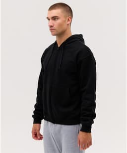 A black zip-up hoodie with a hood and front pockets, modelled by a person wearing grey pants.