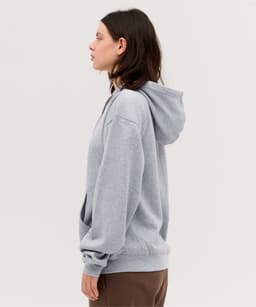 A grey zip hoodie displayed on a model, featuring a hood and a relaxed fit. The hoodie has a logo.