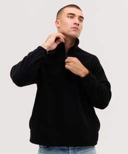 A person wearing a black Everest Polar Fleece 1/4 zip jacket, adjusting the zipper with a neutral background.