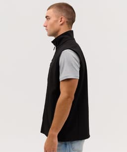 A black softshell vest displayed on a model from the side, featuring a high collar and a branded logo.