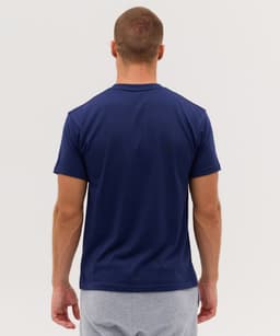 A navy T-shirt viewed from the back, featuring short sleeves and a plain design. The model is wearing grey shorts.