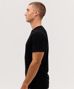 A side view of a man wearing a plain black t-shirt with a logo on the front.