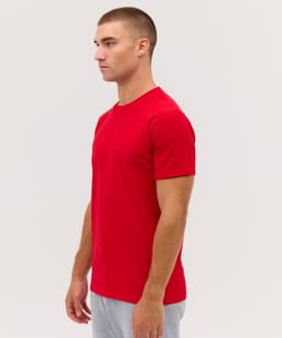 A man in profile wearing a fitted red T-shirt, paired with grey shorts. The shirt features a small logo.