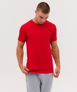 A red t-shirt is worn by a model looking down, paired with grey sweatpants. The shirt features a logo.