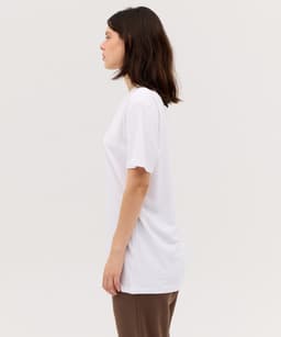 A side view of a woman wearing a plain white T-shirt, showcasing a relaxed fit. The shirt features a logo.