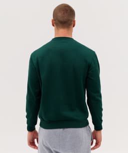 A back view of a man wearing a dark green crew jumper with grey sweatpants, featuring a subtle logo.