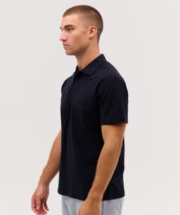 A navy polo shirt with a collar and short sleeves displayed on a model from a side view.