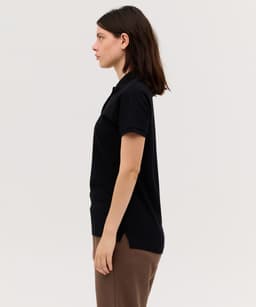 A women's black polo shirt with a subtle logo, displayed on a model in profile view.