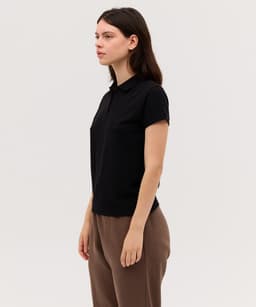 A black women's polo shirt with a classic collar, featuring short sleeves and a fitted silhouette.