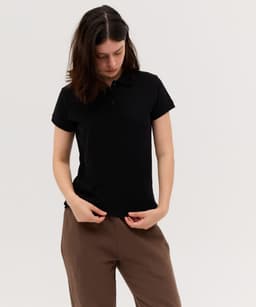 A black women's polo shirt with a collar and short sleeves, displayed on a model. The shirt features a branding logo.