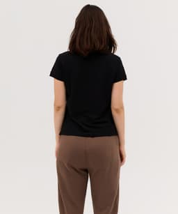 A black women's polo shirt viewed from the back, paired with brown trousers. Features a simple design with a logo.