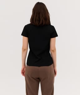 A black women's polo shirt featured from the back, paired with brown pants. It has a simple design and fits snugly.