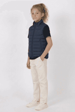 A youth navy puffer vest is worn over a black short-sleeved top, paired with cream trousers and shoes.