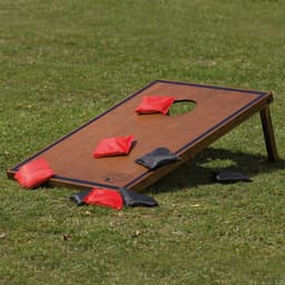 A Backyard Cornhole Set featuring a wooden board and red and black bean bags, placed on grass.