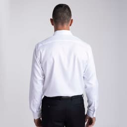 A man wearing a white button-up shirt, viewed from the back, paired with black trousers. The shirt has a logo present.