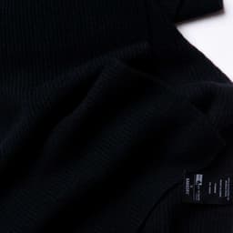 A black 100% Merino scarf, featuring a soft ribbed texture and a label.