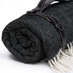 A rolled black and white herringbone picnic blanket secured with a brown strap, featuring fringe edges.