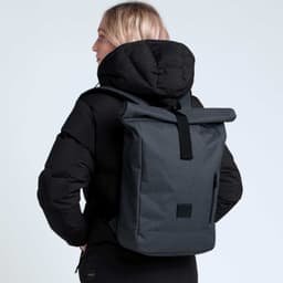 A black and grey roll-top backpack is worn by a person in a black jacket, featuring a logo on the backpack.