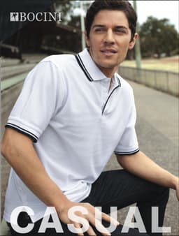 A man wearing a white unisex polo shirt with double black stripes on the collar and sleeves, sitting outdoors.