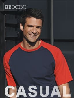 A unisex adults raglan sleeve tee shirt in navy and red with a logo. A smiling model wears the shirt.