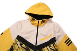 A hooded jacket featuring a yellow and beige design with camouflage patterns and a logo.
