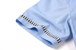 A light blue school shirt with a checkered trim on the hem and sleeves, featuring a brand logo.