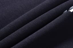 A close-up of a dark navy fabric with a smooth texture, featuring multiple folded layers. It has a subtle sheen.