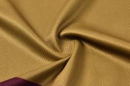 A close-up of a gold fabric with a textured finish, featuring a maroon panel along one edge.