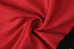 A red and black fabric material, with a textured pattern, twisted to show its softness and flexibility.